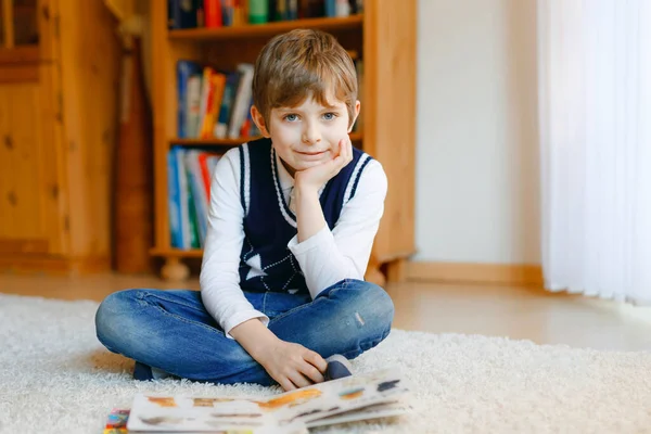 Mignon petit garçon blond lisant le magazine dans la chambre domestique. Enfant excité lisant fort. — Photo