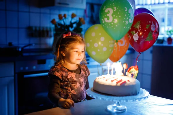 Adorável menina criança comemorando o terceiro aniversário. Criança bebê com bolo de unicórnio caseiro, interior. Criança saudável feliz é surpreendido sobre fogos de artifício sparkler e soprando velas no bolo — Fotografia de Stock