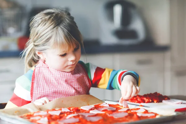 Adorable little toddler girl making italian pizza at home. Cute happy child having fun in home kitchen, indoors. Kid, preschooler helping and preparing healthy meal — Stock Photo, Image