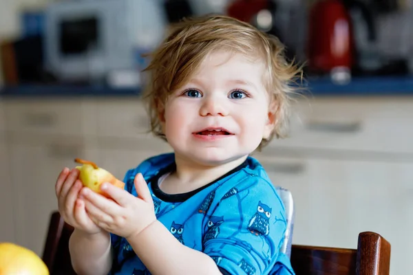Мила чарівна дівчинка, яка їсть свіжу грушу. Голодний щасливий дитина одного року тримає фрукти. Дівчина на домашній кухні, має здорову закуску. Усміхнений блондинка малюк вдома або в розпліднику — стокове фото