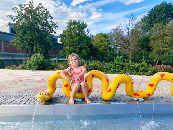 Malé batole dívka cákající ve venkovním bazénu za teplého letního dne. Šťastné zdravé dítě těší slunné počasí ve veřejném bazénu ve městě. — Stock fotografie