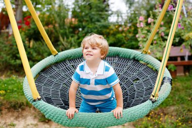 Komik, mutlu anaokulu çocuğu dışarıda zincir salıncak sallıyor. Mutlu gülümseyen çocuk, güneşli yaz gününde oynuyor ve sallanıyor. Çocuklarla aktif zaman geçirme