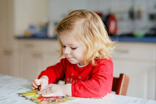 Очаровательная маленькая девочка-блондинка, играющая с головоломками дома или в детском саду. Милый счастливый здоровый ребенок озадачивает и делает картину. Шаг развития и образования для ребенка — стоковое фото