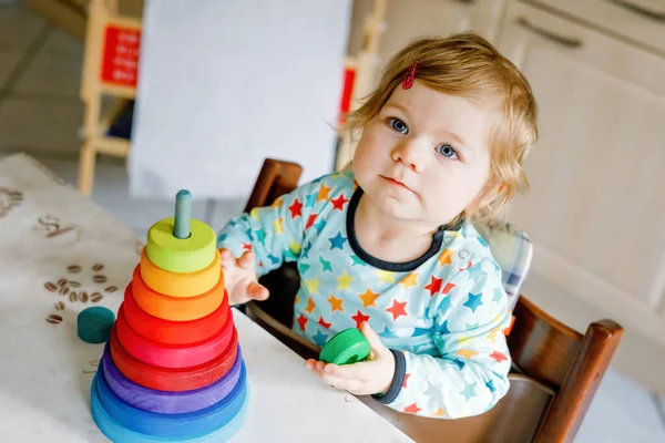 Мила красива маленька дівчинка, яка грає з освітніми іграшками вдома або в дитячій кімнаті. Щаслива здорова дитина розважається з барвистою дерев'яною іграшковою пірамідою веселки. Малюк вивчає різні навички . — стокове фото