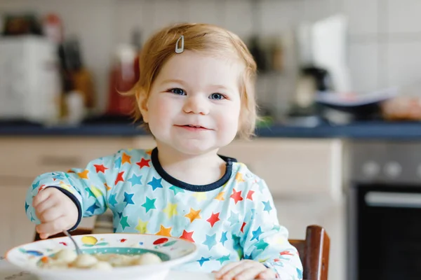 Adorable niña comiendo sopa de fideos vegetales con cuchara. alimento, niño, alimentación y desarrollo. Lindo niño, hija con cuchara sentada en silla alta y aprender a comer por sí mismo. — Foto de Stock