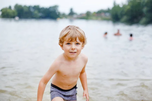 Pequeño niño rubio preescolar divirtiéndose con salpicaduras en un lago en el día de verano, al aire libre. Feliz niño aprendiendo a nadar. Ocio activo con niños de vacaciones. Peligro en lagos domésticos — Foto de Stock