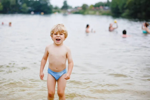 Pequeño niño rubio preescolar divirtiéndose con salpicaduras en un lago en el día de verano, al aire libre. Feliz niño aprendiendo a nadar. Ocio activo con niños de vacaciones. Peligro en lagos domésticos — Foto de Stock