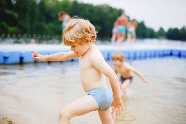 Little blond preschool boy having fun with splashing in a lake on summer day, outdoors. Happy child learning swimming. Active leisure with kids on vacations. Danger on domestic lakes — Stock Photo, Image