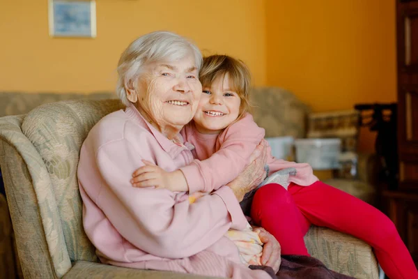 Hermosa niña y bisabuela abrazándose juntas en casa. Lindo niño y mujer mayor divirtiéndose juntos. Familia feliz en el interior — Foto de Stock