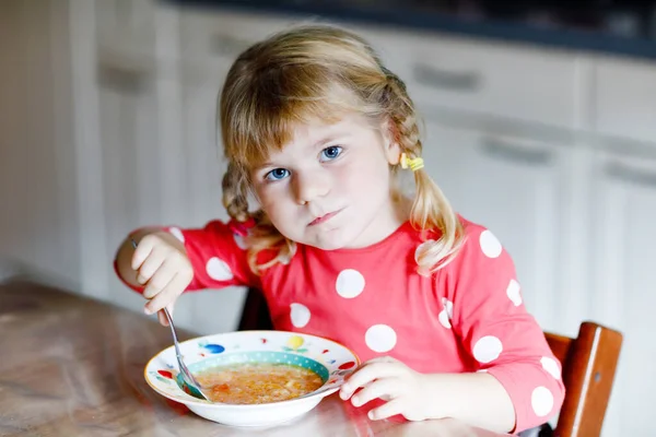 Adorable niñita comiendo sopa de verduras recién cocidas en la cocina. El niño feliz come alimentos saludables para el almuerzo o la cena. Aprendizaje infantil. Hogar, guardería, escuela infantil o guardería — Foto de Stock