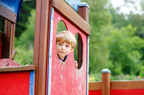 Lindo niño finge conducir un coche imaginario en el patio de niños, al aire libre. Preescolar jugar al aire libre. Chico divirtiéndose con equipo de coche grande. Ocio divertido para los niños en el cálido día de verano —  Fotos de Stock