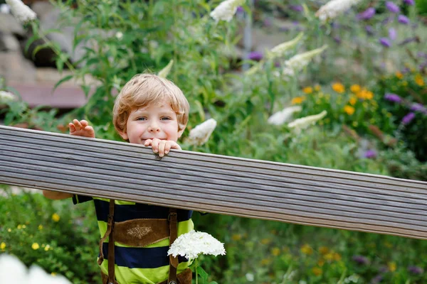 Ritratto di un bel bambino in abiti bavaresi con fiori nella calda giornata estiva soleggiata. Felice bambino sorridente guardando la macchina fotografica. Bambini sani. Tempo libero attivo con i bambini — Foto Stock