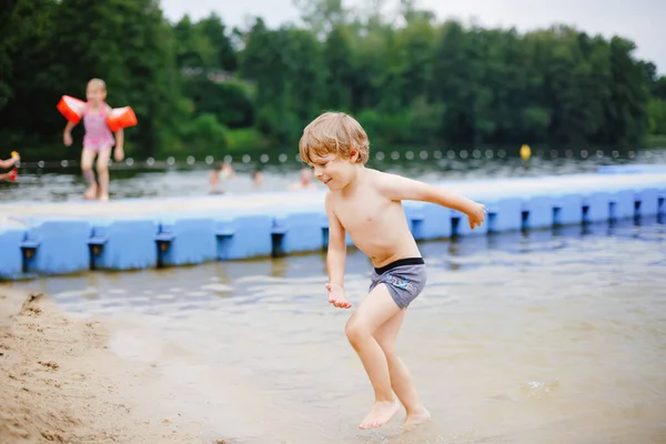 Little blond preschool boy having fun with splashing in a lake on summer day, outdoors. Happy child learning swimming. Active leisure with kids on vacations. Danger on domestic lakes — Stock Photo, Image