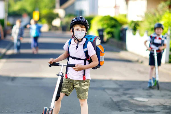 Gözlüklü, sağlık maskeli küçük bir çocuk okula giderken scooterlı. Çantası olan çocuk. Öğrenci çocuk. Corona virüsü salgını sırasında karantina ve karantina süresi. Okulları aç — Stok fotoğraf