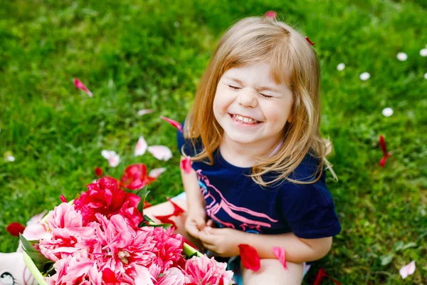 Niedliche entzückende kleine Mädchen mit vielen rosa Pfingstrosen Blumen im Eimer. Glücklich lächelndes Kind im heimischen Garten an warmen Frühlings- oder Sommertagen. — Stockfoto