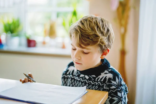 Un ragazzo della scuola felice che lavora sodo facendo i compiti durante la quarantena per una pandemia coronarica. Bambino sano che scrive con la penna, rimanendo a casa. Concetto di istruzione a casa — Foto Stock