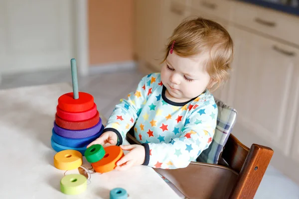 Bonito linda menina brincando com brinquedos educativos em casa ou berçário, dentro de casa. Criança saudável feliz se divertindo com pirâmide de brinquedo colorido arco-íris de madeira. Aprendizagem de crianças habilidades diferentes. — Fotografia de Stock