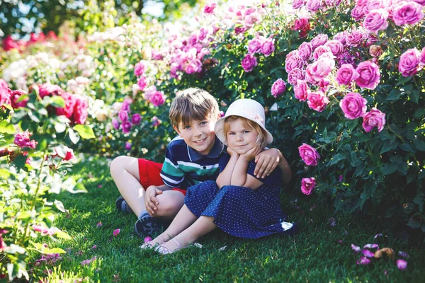 Retrato de menina pequena criança no jardim de rosas florescendo. Bonito linda criança se divertindo com rosas e flores em um parque no dia ensolarado de verão. Feliz bebê sorridente. — Fotografia de Stock
