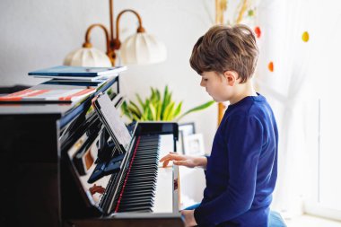 Güzel küçük çocuk oturma odasında piyano çalıyor. Çocuk, müzik enstrümanını tablet uygulaması ile çalmayı öğrenirken eğleniyor. Evde eğitim gören korona virüsü kilitlenmesi sırasında e-öğrenim kavramı.