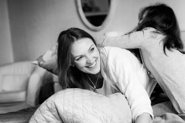 Madre cariñosa y niña escolar haciendo peleas de almohadas juntos. Familia feliz, mujer y linda hija divirtiéndose juntos en la cama. Cuidado familiar, rutas matutinas y estilo de vida. —  Fotos de Stock