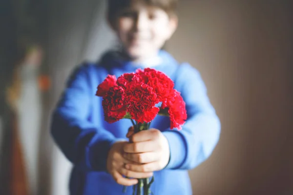 Närbild av händerna på en ung pojke som håller i en massa kryddnejlika blommor. Barn gratulerar och presenterar Kryddnejlikor till mor eller flicka vän för mödrar dag eller Alla hjärtans dag. — Stockfoto