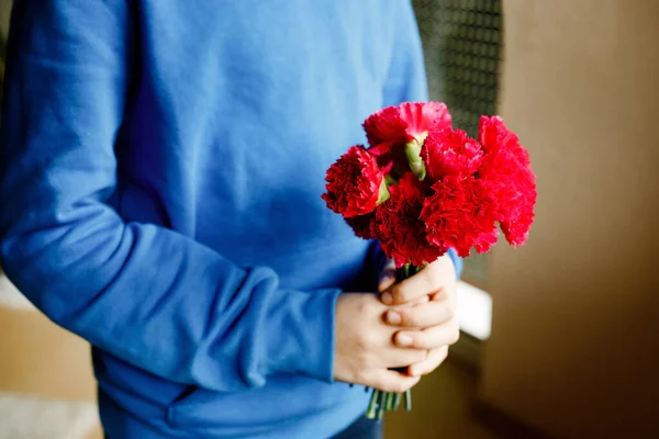 Närbild av händerna på en ung pojke som håller i en massa kryddnejlika blommor. Barn gratulerar och presenterar Kryddnejlikor till mor eller flicka vän för mödrar dag eller Alla hjärtans dag. — Stockfoto