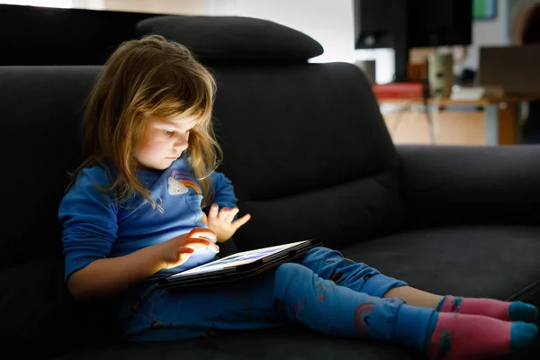 Carino bambina bambino che gioca con tablet pc a casa. Sano bambino toccando pad con le dita, cercando cartoni animati e divertirsi con applicazioni educative. Bambino in pigiama biancheria da notte sentire audiolibro — Foto Stock