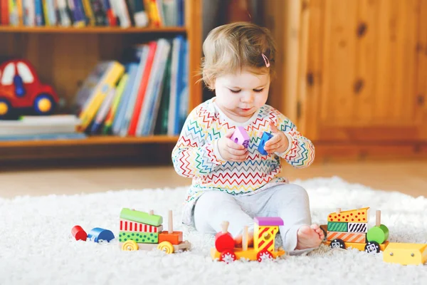 Malá holčička hrající si se vzdělávacími dřevěnými hračkami doma nebo v jeslích. Batole s barevným vláčkem. Dítě se baví s různými hračkami. Osamělé dítě během pandemické karantény viru korony — Stock fotografie
