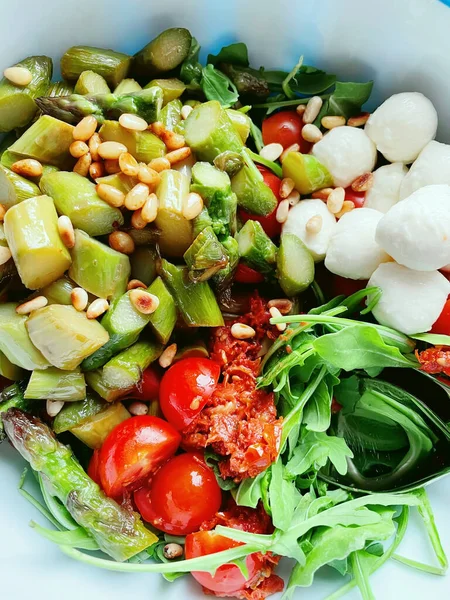 Fresh vegeratian salad with green asparagus, mozarella, tomatoes, arugula and pine nuts. Healthy lunch food or salad for barbecue. Top view. — Stock Photo, Image