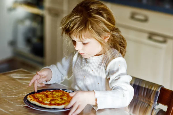 Söt liten flicka äter italiensk pizza med grönsaker och ostar. Glada barn äter färsk kokt hälsosam måltid med tomater, majs och grönsaker hemma, inomhus. — Stockfoto