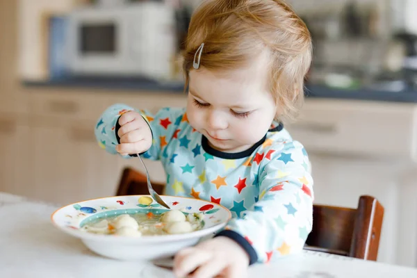 Entzückendes kleines Mädchen, das von einer löffelweise Gemüsenudelsuppe isst. Ernährung, Kind, Ernährung und Entwicklungskonzept. Niedliches Kleinkind, Tochter mit Löffel sitzt im Hochstuhl und lernt selbst zu essen. — Stockfoto