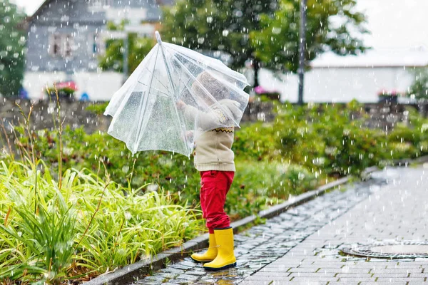 Pequeño niño rubio caminando con un gran paraguas al aire libre en el día lluvioso. Niños en edad preescolar que se divierten y usan ropa impermeable colorida y botas de goma de goma de lluvia. Ocio al aire libre en mal tiempo día — Foto de Stock