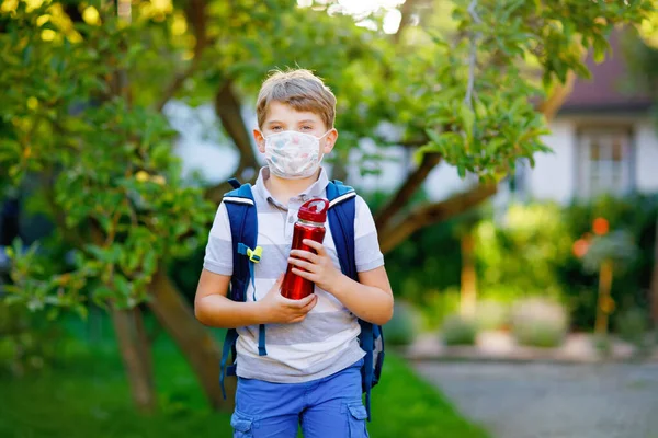 Niño feliz con máscara médica y mochila. Un colegial de camino a la escuela. Un niño sano al aire libre. Regreso a la escuela después de la cuarentena del bloqueo de la enfermedad pandémica de corona — Foto de Stock