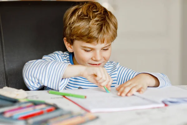 Retrato de lindo niño feliz escuela sana en casa haciendo tarea. Niño pequeño escribiendo con lápices de colores, en el interior. Escuela primaria y educación. Niño aprendiendo a escribir letras y números — Foto de Stock