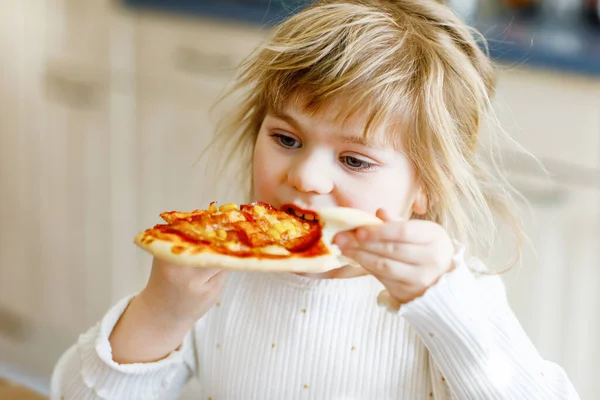 Menina da criança adorável comer pizza italiana com legumes e queijos. Criança feliz comendo refeição saudável cozida fresca com tomate, milho e legumes em casa, dentro de casa. — Fotografia de Stock