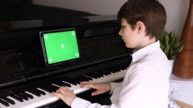 Liseli çocuk tablet uygulaması ile piyano çalmayı öğreniyor. Çocuk müzik aleti çalmayı öğrenirken eğleniyor. Yeni uygulama, ticaret ve programlar için yeşil ekran krom anahtar arka planına sahip tablet