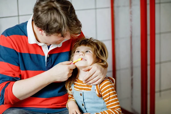 Отец помогает своей маленькой дочери чистить зубы. Маленькая девочка и папа в ванной, занимаются гигиеной. Счастливая семья, мужчина и ребенок. Утренняя программа с детьми. — стоковое фото