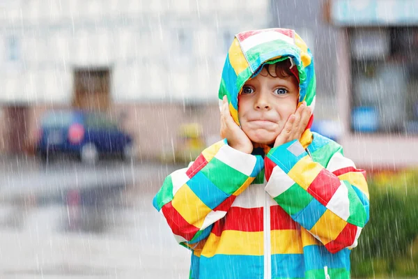 Porträtt av en liten pojke som leker på regnig dag. Glad positiv barn har kul med att fånga regndroppar. Grabben med regnkläder. Barn och familj utomhus aktivitet på dåligt väder dag. — Stockfoto