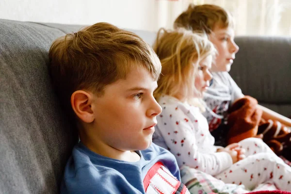 Aranyos kislány és két iskolás fiú rajzfilmeket vagy filmet néznek a tévében. Három boldog, egészséges gyermek, testvérek a koronavírus karantén alatt, akik otthon maradnak. Testvérek együtt.. — Stock Fotó