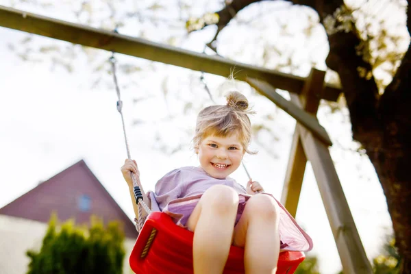 Happy little toddler girl having fun on swing in domestic garden. Smiling positive healthy child swinging on sunny day. Preschool girl laughing and crying. Active leisure and activity outdoors. — Stock Photo, Image