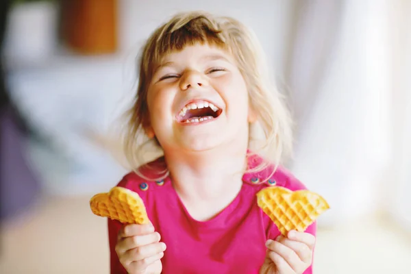 Retrato da menina pré-escolar feliz segurando waffle coração fresco cozido. Criança com fome sorridente com bolacha doce. Açúcar doce waffles belgas. — Fotografia de Stock