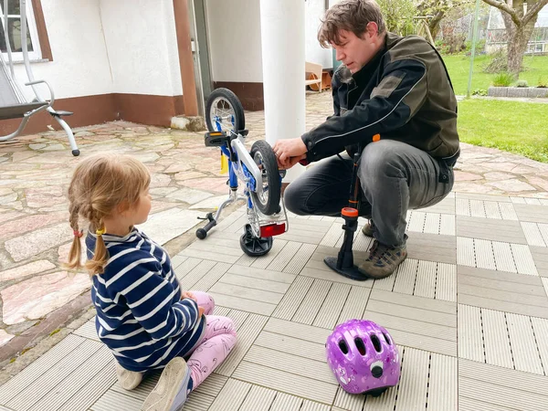 Pequeña niña preescolar y padre cadena de reparación en bicicleta e inflar neumáticos de bicicleta. Niño y papá trabajan juntos. Familia al aire libre. Ocio activo. Hija y papá tiempo. Niño aprendiendo del hombre —  Fotos de Stock