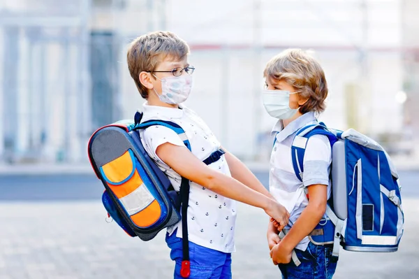 Dos niños con máscara médica camino a la escuela. Niños con mochilas. Los colegiales en un día cálido y soleado. Tiempo de bloqueo y cuarentena durante la enfermedad pandémica de corona — Foto de Stock