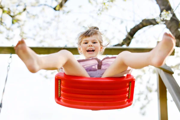 Glad liten småbarn flicka som har kul på swing i hushållsträdgården. Leende positiva friska barn svänger på solig dag. Förskoleflickan skrattar och gråter. Aktiv fritid och aktivitet utomhus. — Stockfoto