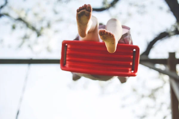 Closeup of feet of little toddler girl having fun on swing in domestic garden. Small child swinging under blooming trees on sunny day. Active leisure and activity outdoors