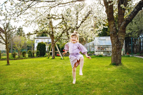 Felice bambina che si diverte a giocare in giardino domestico. Sorridente bambino sano positivo correre e saltare sul cortile. Ragazza in età prescolare ridere e piangere. Tempo libero attivo e attività all'aperto — Foto Stock