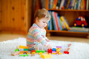 Küçük kız evde ya da çocuk odasında eğitici tahta oyuncaklarla oynuyor. Renkli trenle yürüyen çocuk. Çocuk farklı oyuncaklarla eğleniyor. Korona virüsü salgını sırasındaki yalnız çocuk karantina