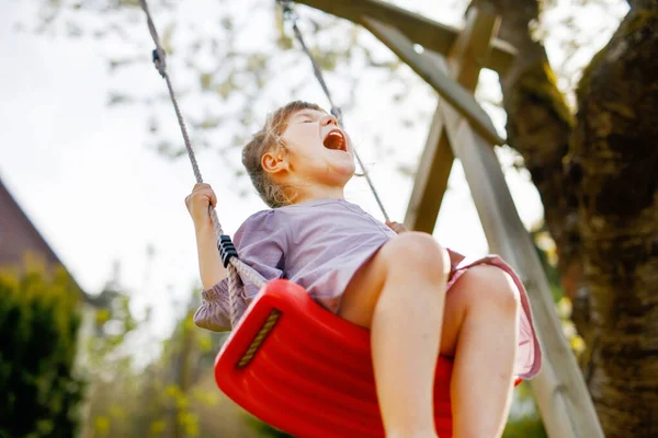 Šťastné malé batole dívka baví na houpačce v domácí zahradě. Usmívající se zdravé dítě houpající se za slunečného dne. Holka ze školky se směje a brečí. Aktivní volný čas a aktivita venku. — Stock fotografie