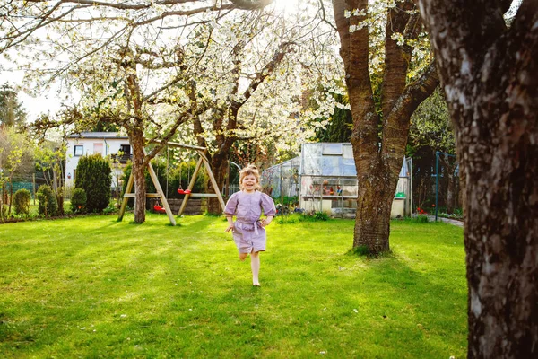 Šťastné malé batole dívka baví s hraní v domácí zahradě. Usmívající se zdravé dítě běžet a skočit na dvorek. Holka ze školky se směje a brečí. Aktivní volný čas a aktivita venku — Stock fotografie