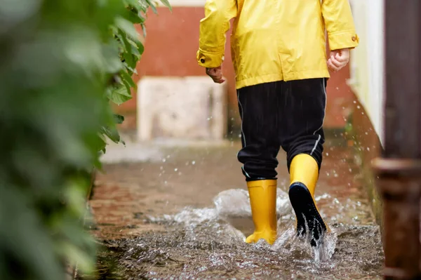 Close-up de criança vestindo botas de chuva amarelas e caminhando durante o trenó, chuva e neve no dia frio. Criança de forma colorida roupas casuais pulando em uma poça. Divertir-se ao ar livre — Fotografia de Stock